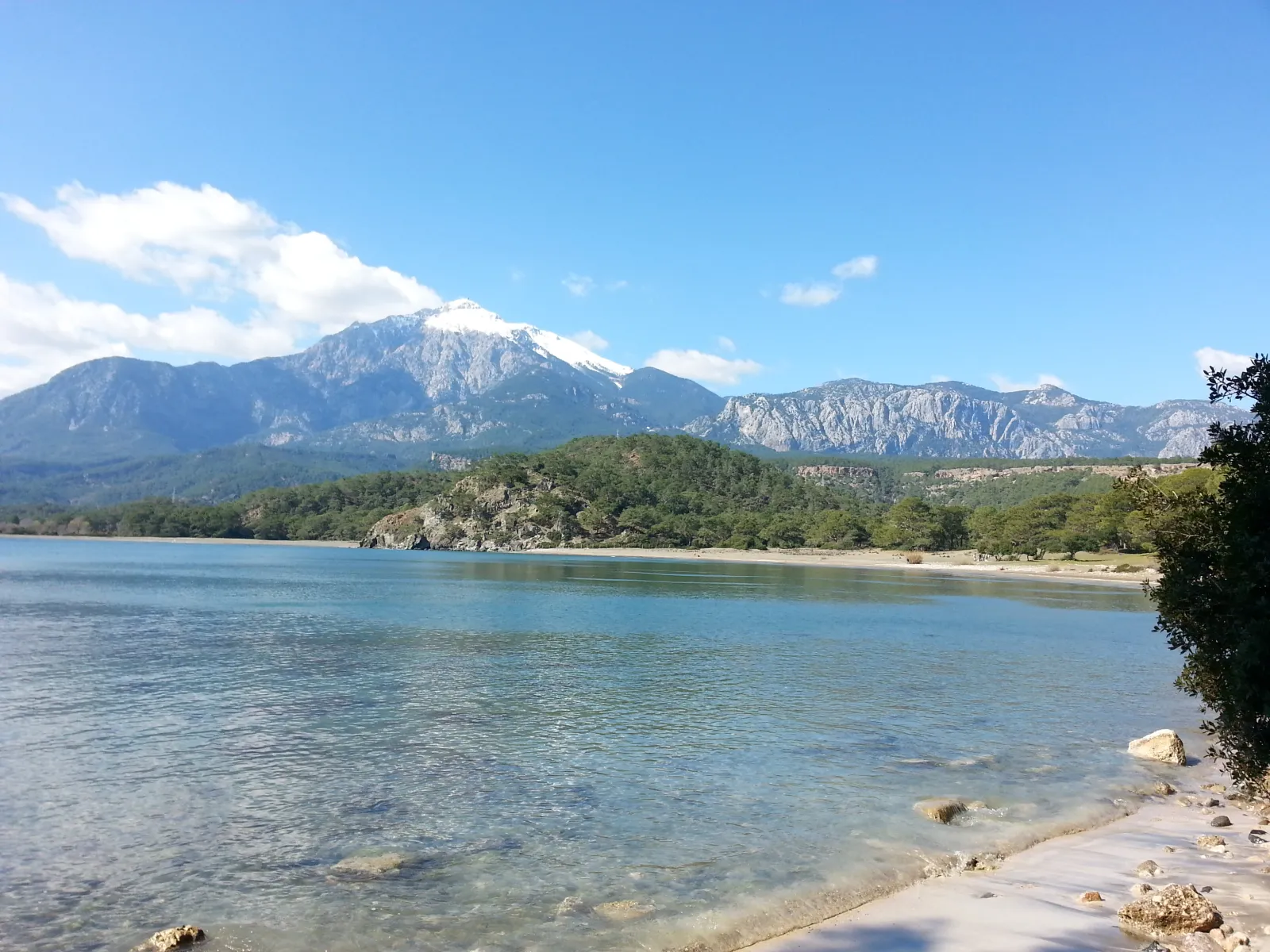 Çıralı kıyısından berrak deniz ve arkada karla kaplı Tahtalı Dağı