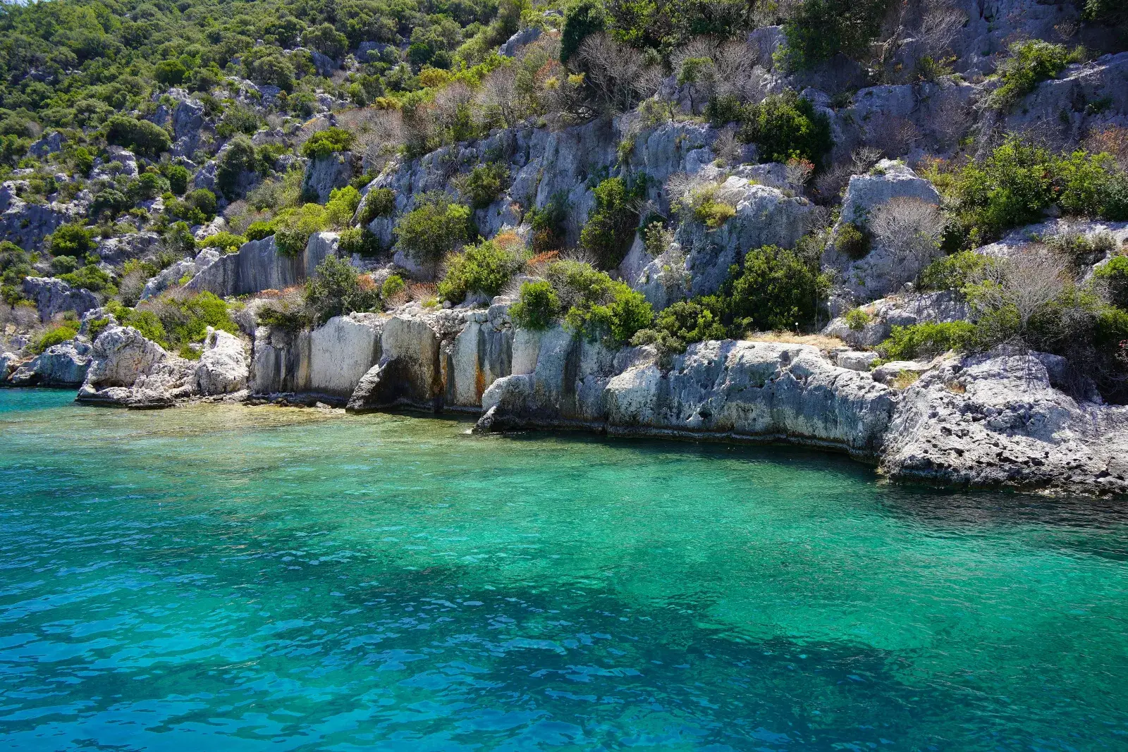 Kekova'da turkuaz suyun kıyısında kayalara oyulmuş batık şehir kalıntıları