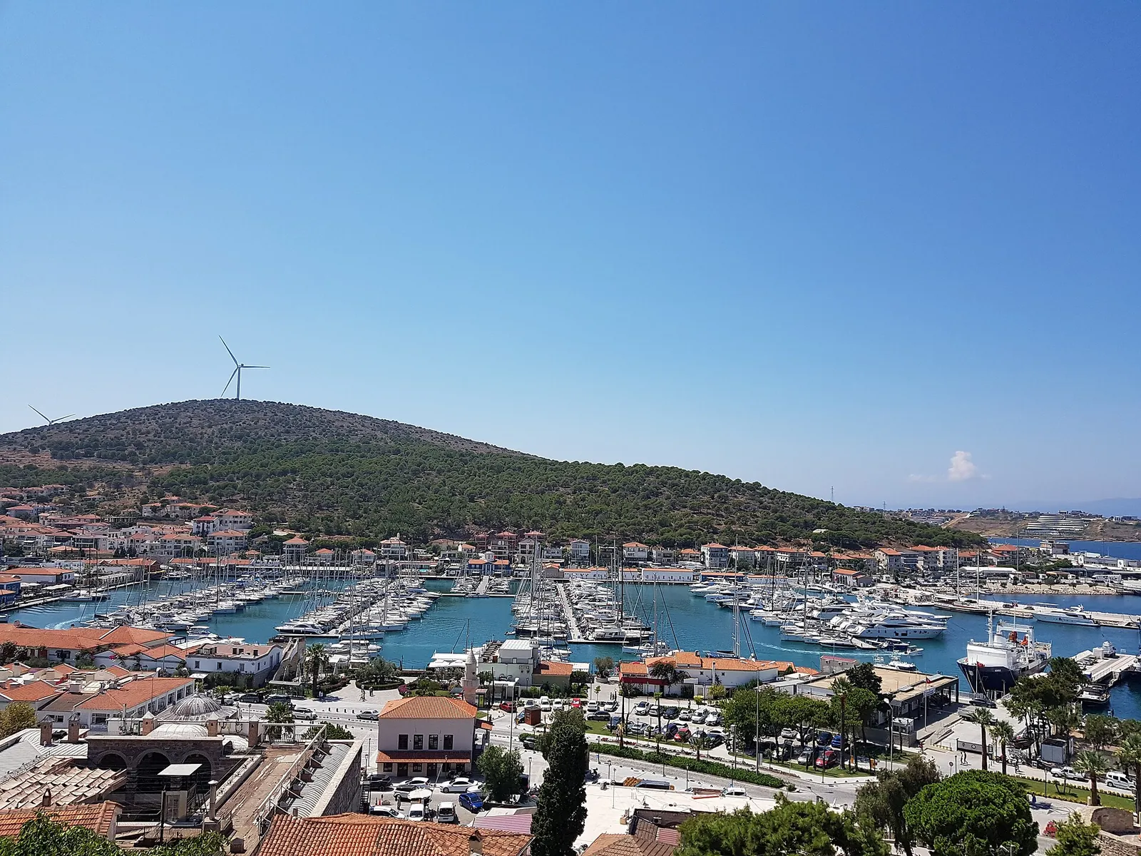Çeşme yat limanı, kıyıdaki evler ve rüzgâr türbinli tepe